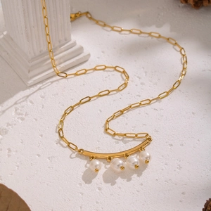 Détail d'un collier chaîne trombone dorée avec quatre perles blanches sur une barre courbée