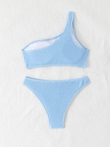 Light blue smocked one-shoulder bikini set displayed on a white textured towel background