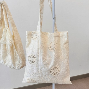 Detail of delicate floral embroidery on cream-colored lace canvas tote bag surface