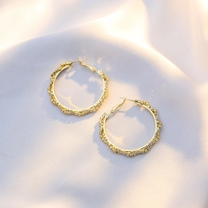 Close-up of gold hoop earrings with sparkling white cubic zirconia on silk fabric
