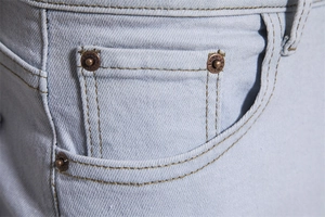 Detail view of denim jeans front pocket with metal rivets and precise stitching