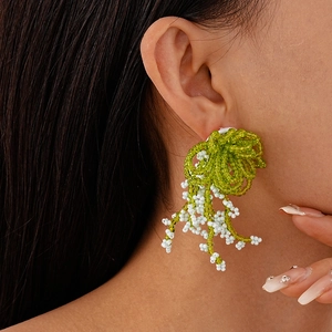 Detail of handmade green and white beaded lily of the valley earrings worn by a model