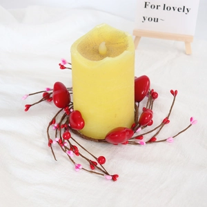 Detail of red heart berry candle ring wreath around a yellow pillar candle on white fabric