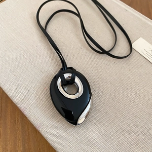 Detail of teardrop pendant necklace with black resin and silver metal on a book