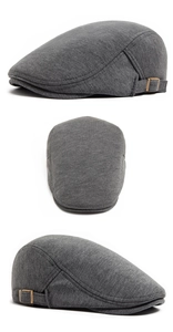 Detail of dark grey knit newsboy cap showing bronze metal buckle and side stitching
