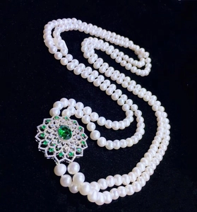 Macro view of double-layer pearl necklace featuring a floral clasp with green gemstone
