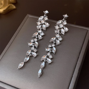 Macro detail of silver tassel earrings with sparkling crystals on a textured jewelry box