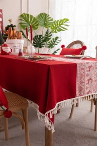 Close-up of red Christmas tablecloth featuring white reindeer patterns and fringe trim