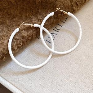 Detailed view of large round hoop earrings with white leather wrap and gold metal clasps