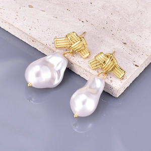 Elegant gold knot earrings with white baroque pearl pendants on a textured stone base