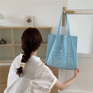 Detail einer hellblauen Canvas-Tasche mit Bébé-Stickerei am Türgriff aufgehängt