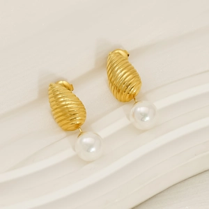 Gros plan de boucles d'oreilles perles avec métal doré texturé sur tissu blanc