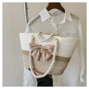Detail of hand-woven straw tote bag featuring a large champagne satin bow and rope handles
