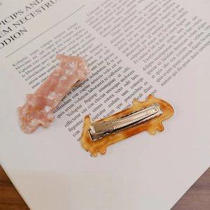 Kawaii cat-shaped hair clips in pink floral and amber acetate on a book background