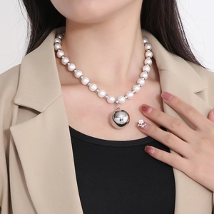 Detail of a white pearl necklace with a large silver spherical pendant on a model neck