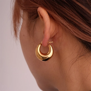 Close-up of golden chunky hoop earrings worn by a model for a modern minimalist look
