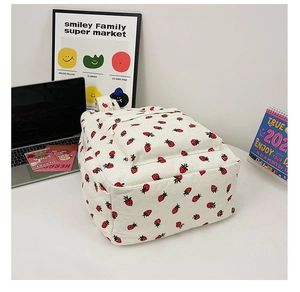 Detail of off-white corduroy backpack with red strawberry print on a minimalist desk