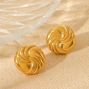 Macro shot of gold spiral textured circular stud earrings on beige linen background