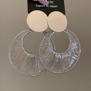 Detailed close-up of large silver circular earrings with intricate wire-wrapped texture