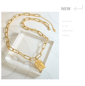 Detail view of golden paperclip chain with rectangular face relief pendant and matte texture