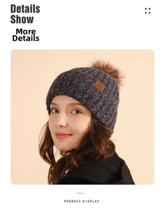 Detailed close-up of dark knit beanie with brown faux fur pom and snowflake leather patch