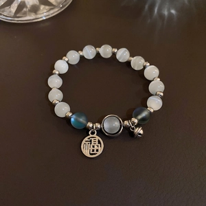 Detailed close-up of beaded opal bracelet with silver bell and Fu character charm
