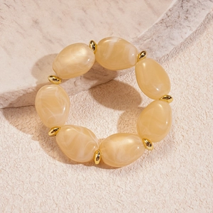 Detailed shot of cream acrylic oval beaded bracelet with gold accents on stone base