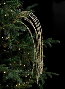 Detail van een sprankelende gouden lovertjes tak in een kerstboom met warme lichtjes