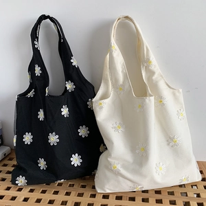 Close-up of embroidered daisy patterns on black and white canvas tote bags