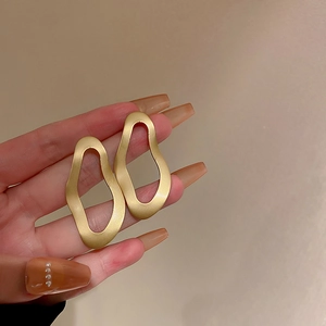 Detailansicht unregelmäßiger goldener geometrischer Ohrstecker in der Hand gehalten