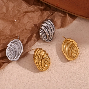 Macro detail of wave textured button earrings in gold and silver finish on paper