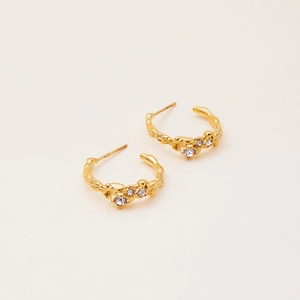 Detailed macro view of C-shaped golden earrings with textured lava finish and purple gems