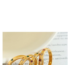 Close-up of four gold rings with colorful gemstones leaning against a ceramic cup