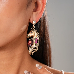 Macro shot of retro gold horse earrings with red crystal and sparkling diamond accents
