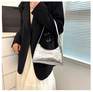 Silver crocodile pattern baguette bag worn on the shoulder in a minimalist indoor setting