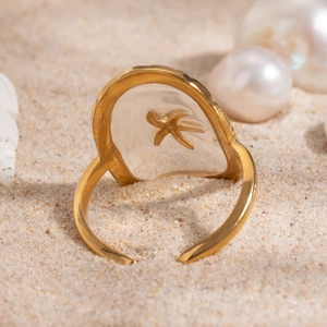 Macro view of adjustable gold starfish ring with resin detail on a beach sand background