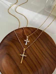 Detailed view of two gold cross pendants with zircons on a wooden tray display