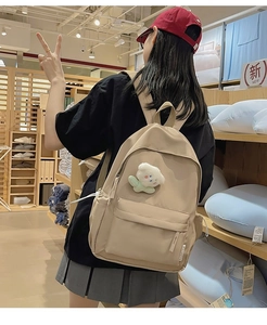 Detail of beige nylon backpack with front pocket and cute white plush flower charm