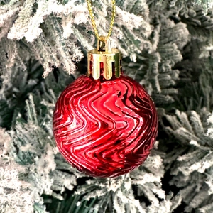 Close-up of red wavy textured Christmas ball ornament hanging on a snowy pine tree branch