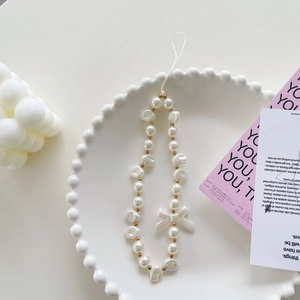 Detail of white pearls and bow charm on phone lanyard in a minimalist ceramic tray