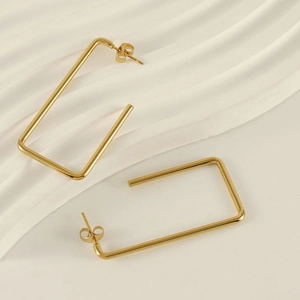 Macro view of geometric rectangular gold earrings on soft fabric with metal texture