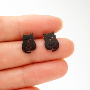 Nahaufnahme kleiner schwarzer Katzen-Ohrstecker auf dem Finger zur Größenansicht