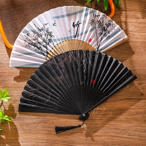 Traditional Chinese folding fans with bamboo ink painting and black tassel on wood desk