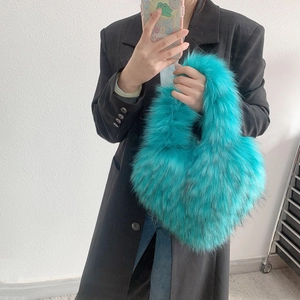 Close-up of fluffy turquoise faux fur handbag held by model wearing a black blazer