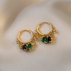 Close-up of gold hoop earrings with multi-colored gemstone charms on silk fabric