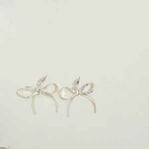 Detailed view of silver bow earrings with a textured finish on a neutral background