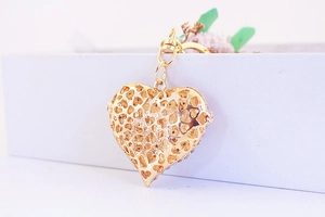 Detailed view of an openwork heart-shaped locket keychain in a polished golden metal finish