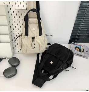 Detail view of lightweight nylon sling bags in beige and black on white pegboard