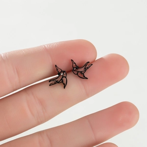 Close-up detail of bird-shaped stud earrings in matte black held between fingers