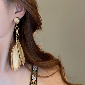 Close-up of elegant gold feather drop earrings with textured disc studs on model